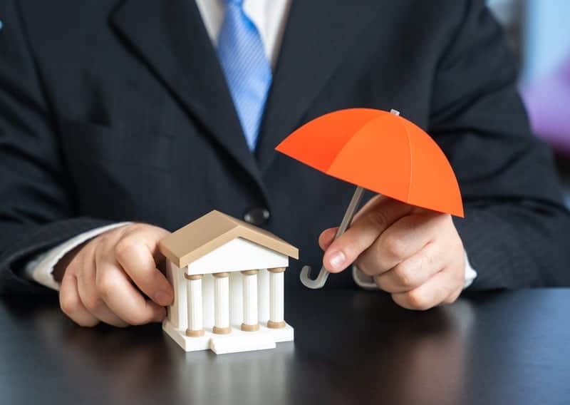 Businessman holding umbrella over bank model